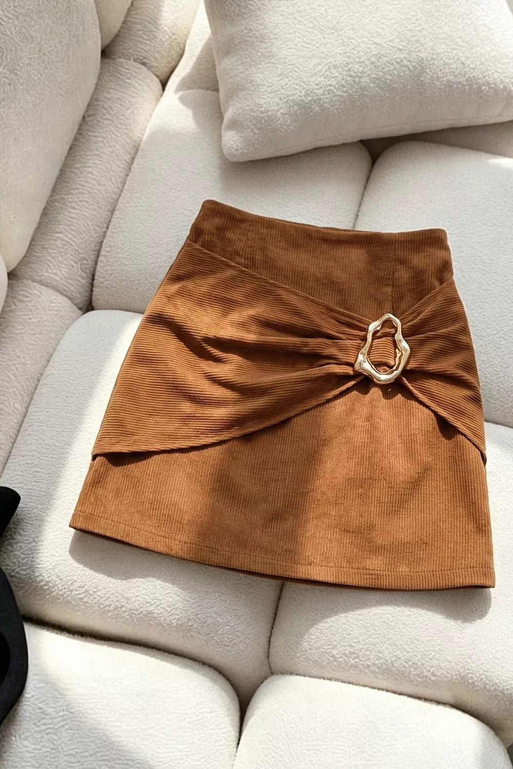 Women's caramel ruched mini skirt with gold-tone metal buckle, draped front and textured fabric finish.