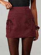 Women's burgundy mini skirt featuring decorative side bow ties, short hemline and tailored silhouette.