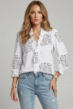 Women's white V-neck ruffle blouse with black script print and button-front styling.